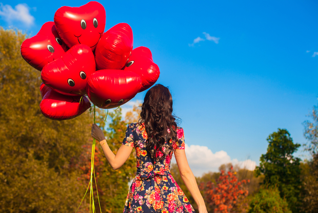 Woman wears floral dress and holds smiley balloons Woman wears floral dress and holds smiley balloons