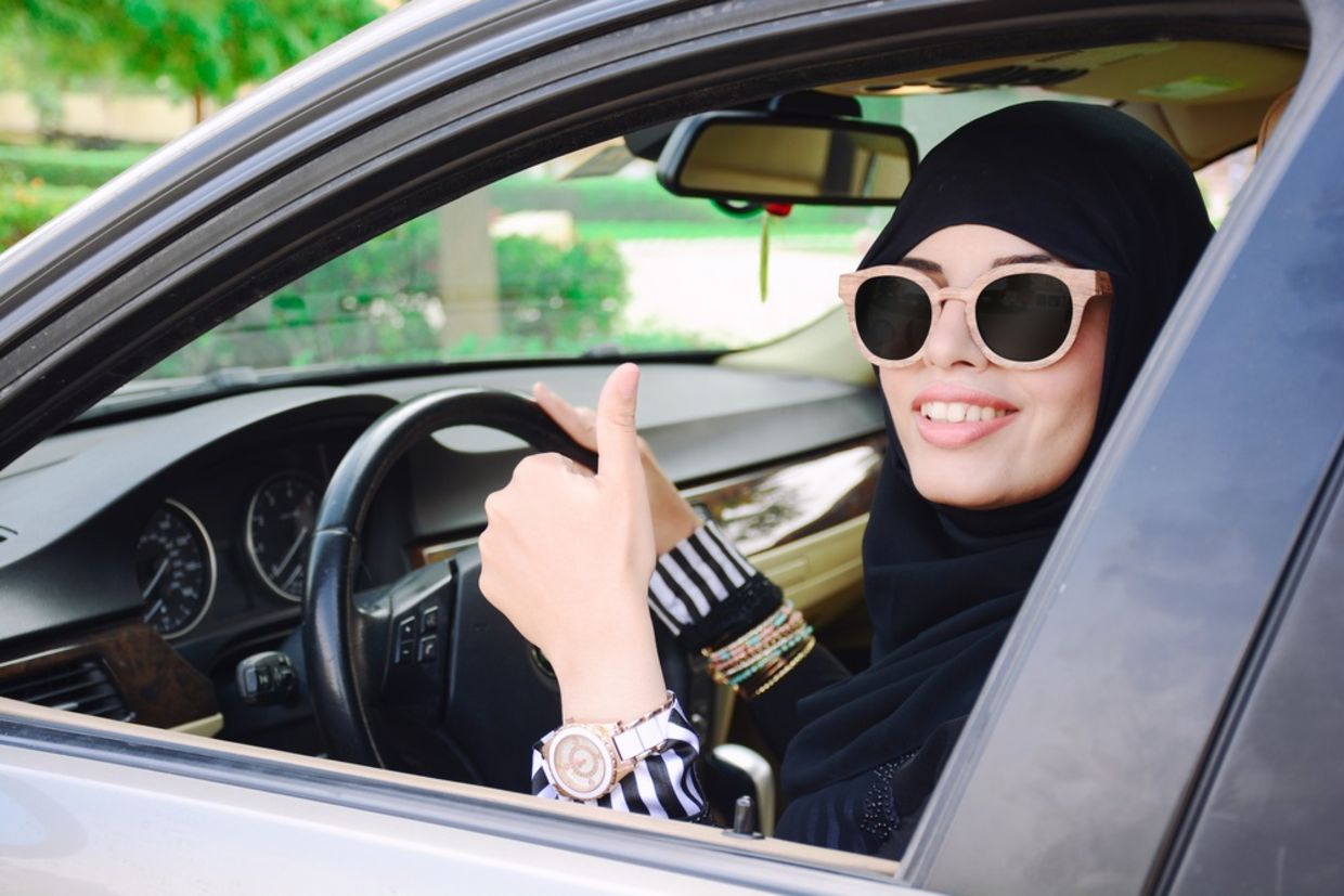 Happy business arabic lady in dark abaya and hijab driving her car and showing thumb up. Smiling arabian lady in sunglasses taking steering wheel of her new car. Happy business arabic lady in dark abaya and hijab driving her car and showing thumb up. Smiling arabian lady in sunglasses taking steering wheel of her new car.