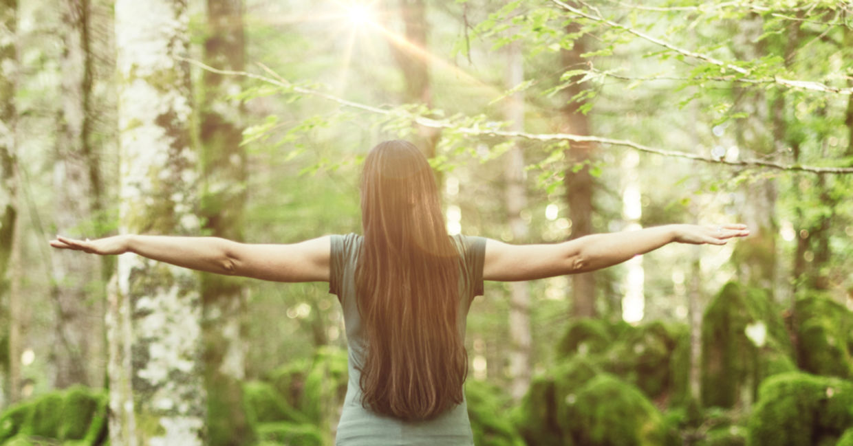 A woman in a forest spreads her arms out wide, showing balance and harmony. A woman in a forest spreads her arms out wide, showing balance and harmony.