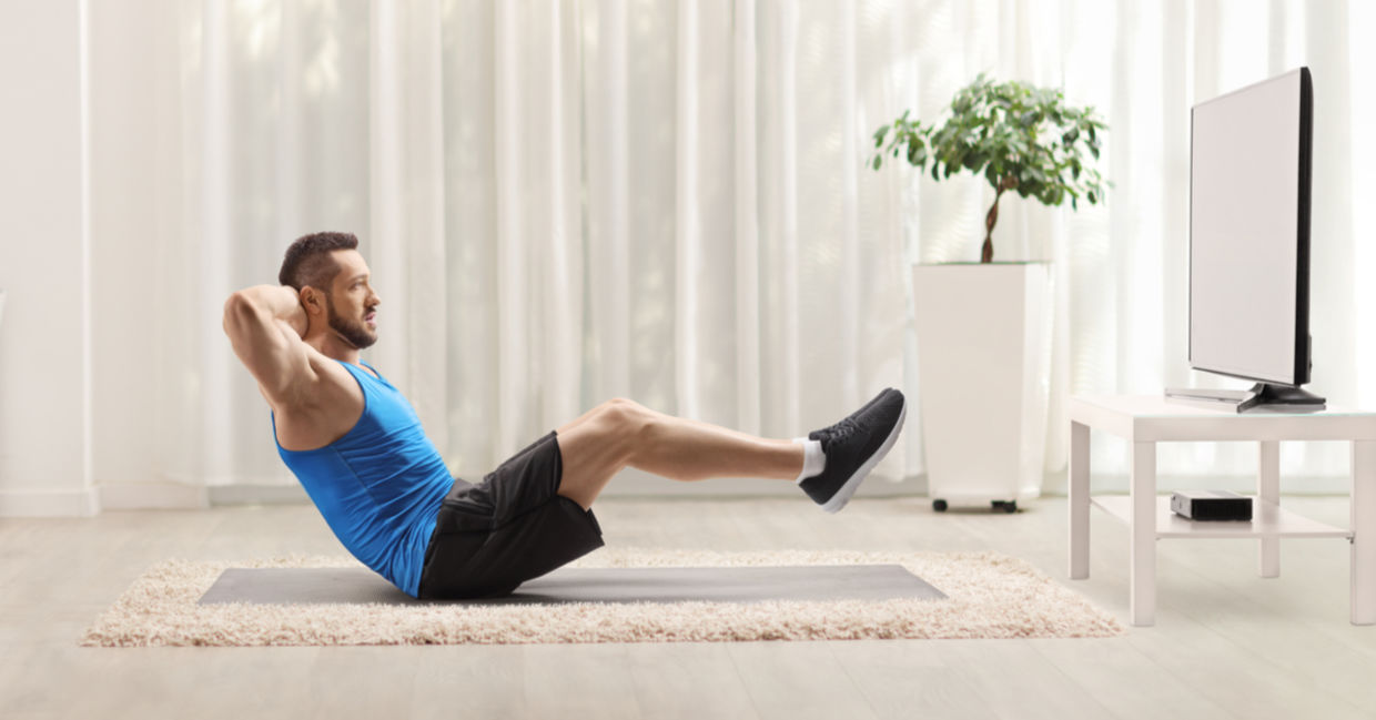 A man is doing sit ups in front of the TV. A man is doing sit ups in front of the TV.