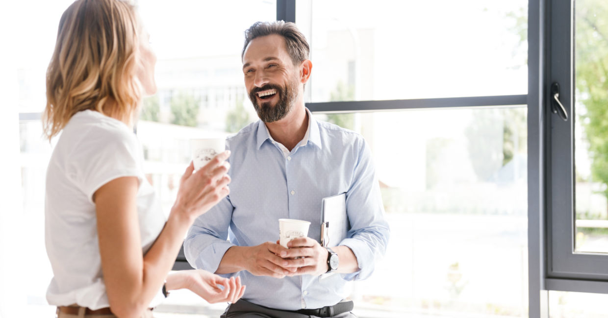 Happy colleagues talking while standing at the office window Happy colleagues talking while standing at the office window