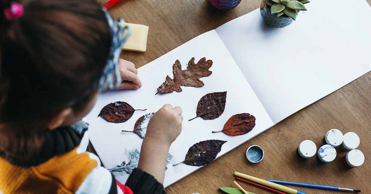 A child pastes dried leaves on a white album sheet A child pastes dried leaves on a white album sheet