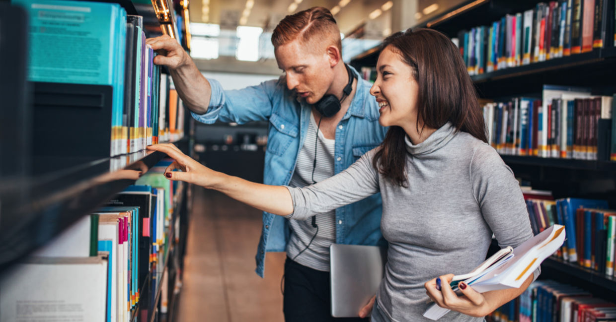 Two young students getting books from a public library shelf. Two young students getting books from a public library shelf.