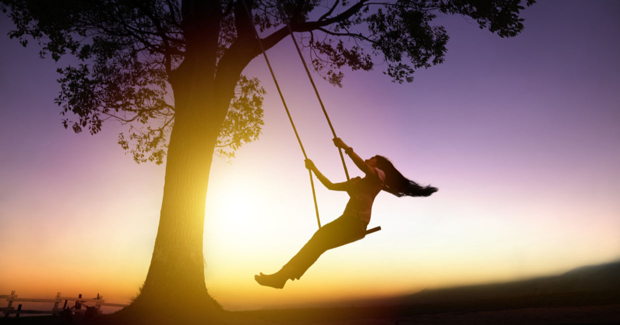 Silhouette of joyful woman on a swing with sunset background Silhouette of joyful woman on a swing with sunset background