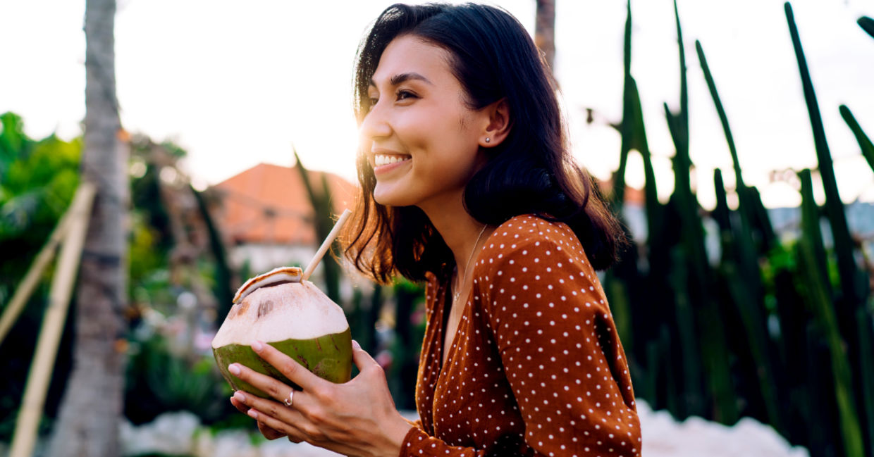 Woman enjoying a coconut water drink through a straw on a sunny evening. Woman enjoying a coconut water drink through a straw on a sunny evening.
