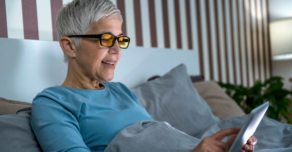 A woman wears blue light blocking glasses to look at her tablet. A woman wears blue light blocking glasses to look at her tablet.