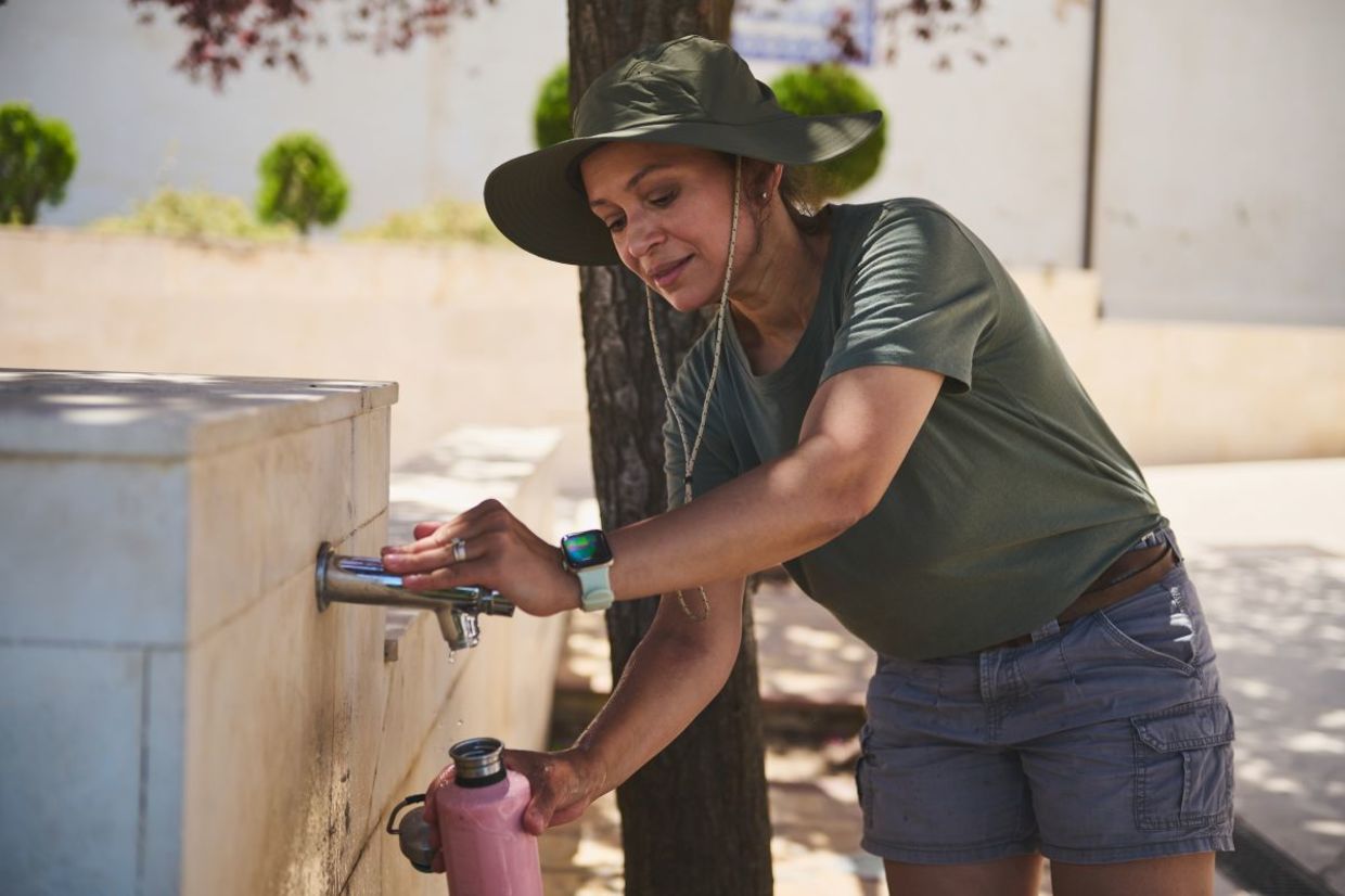 A woman refilling her reusable water bottle. A woman refilling her reusable water bottle.
