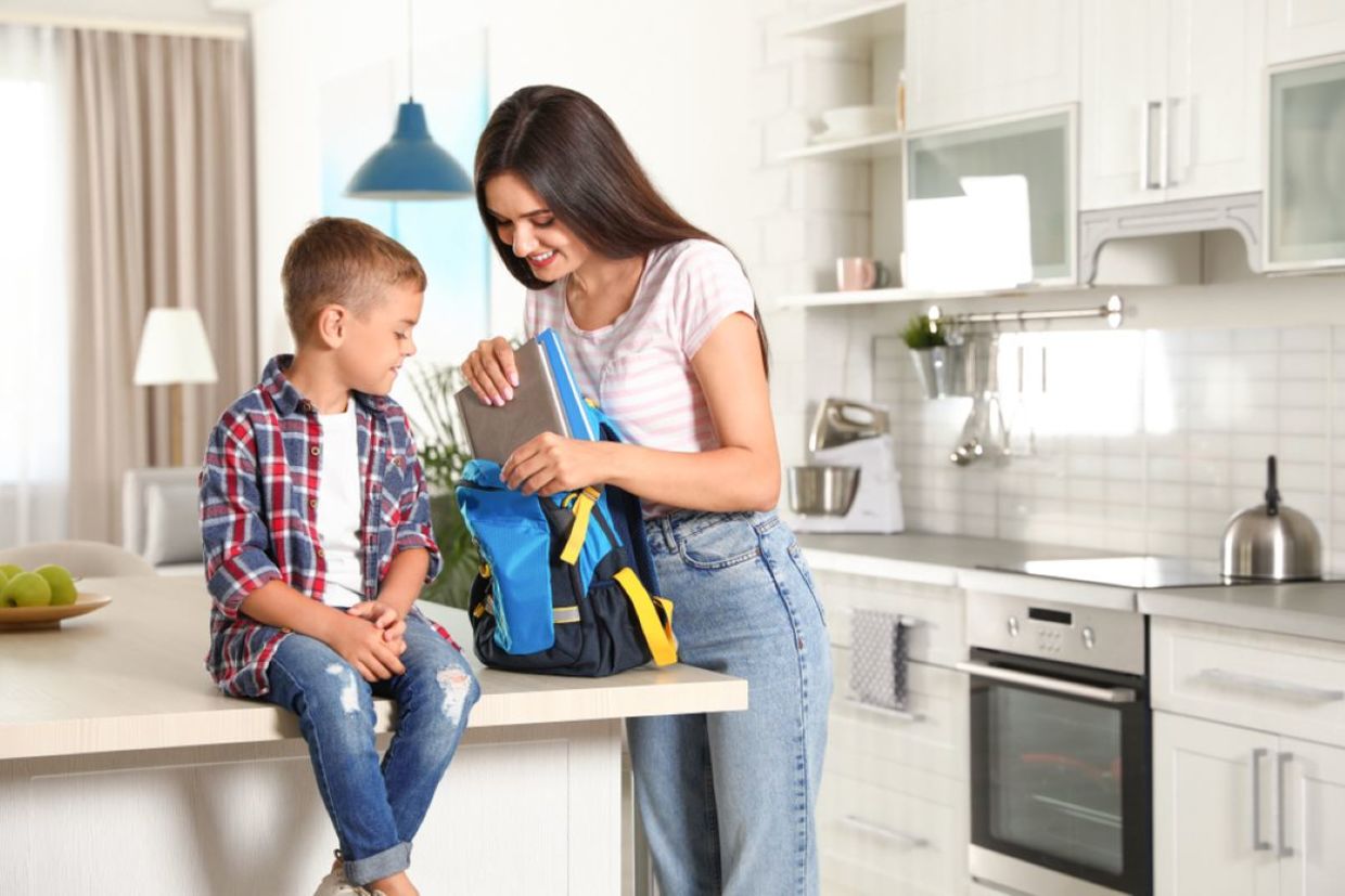 A smiling mother helps her son pack a backpack. A smiling mother helps her son pack a backpack.